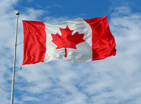 The Canadian flag flutters against a partially cloudy sky