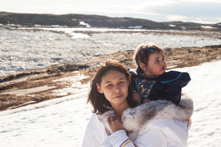 Femme inuite portant un enfant sur son dos pour traverser la toundra enneigée