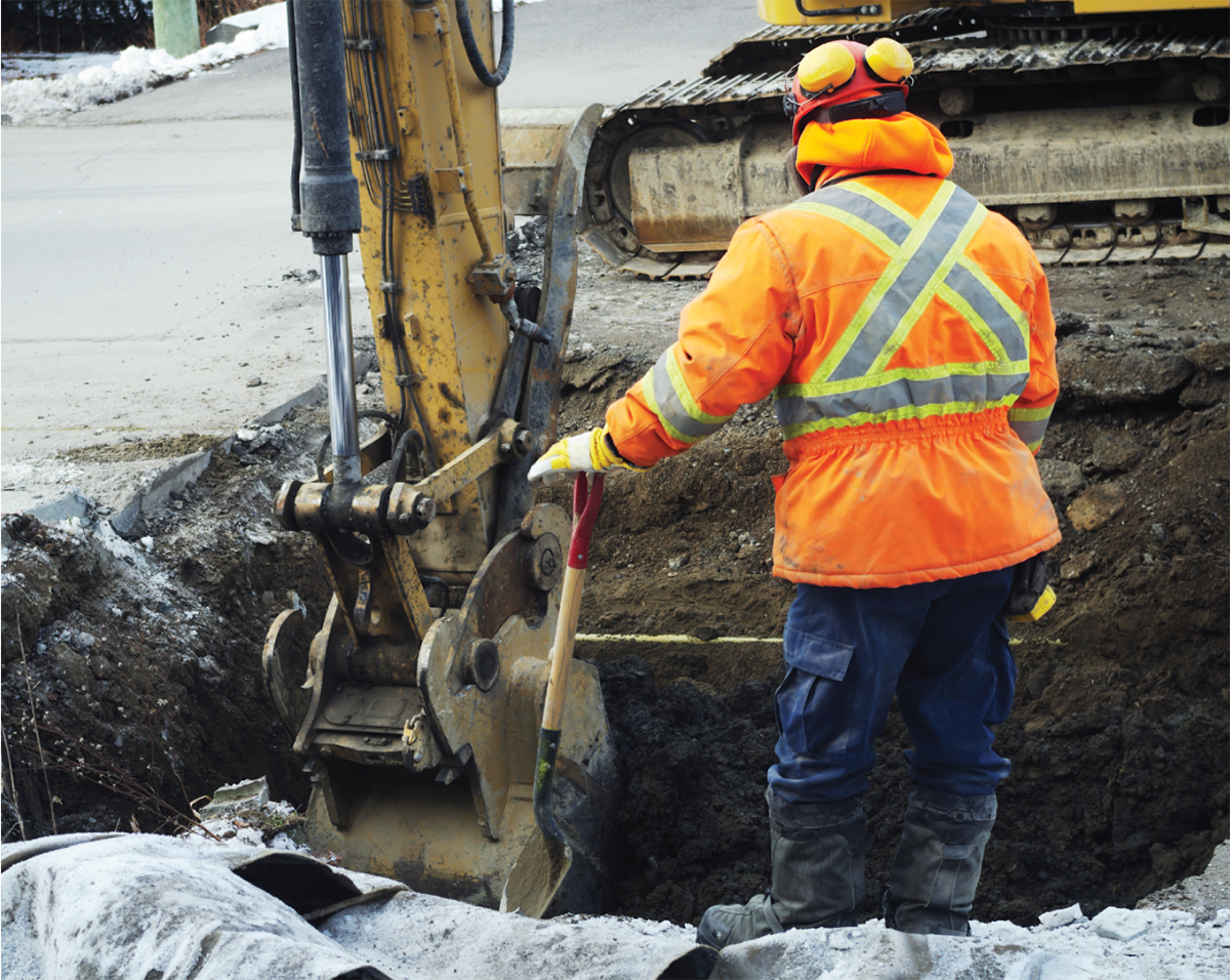 Travailleur de la construction devant une excavatrice effectuant des travaux de réparation sur une route